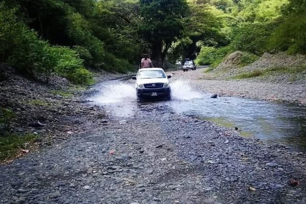98979727-d5bf-433d-a1fa-9d678623cef4 4x4 off-road vehicle driving through shallow river on Tobago rainforest tour.